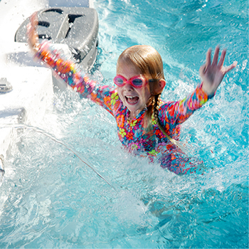 Un enfant souriant, les mains en l'air, flottant dans un spa de nage.