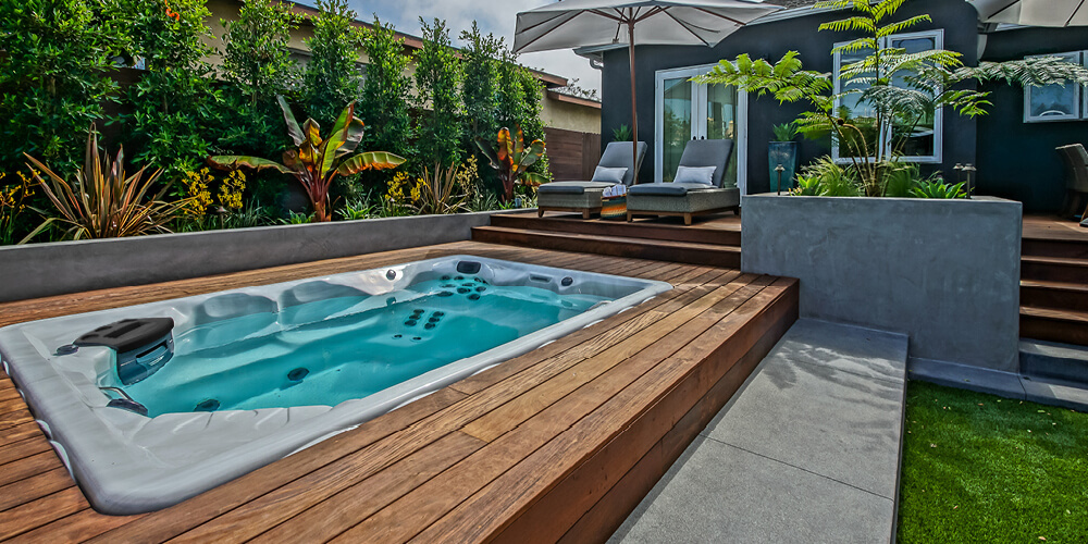 Des parasols et des transats disposés autour d'un spa de nage Therapool.