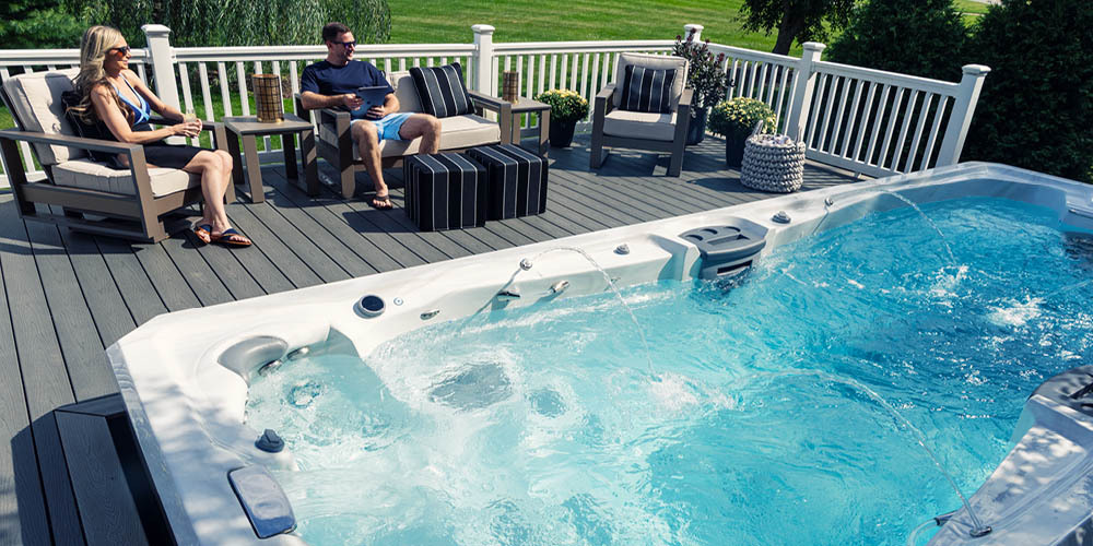 Un couple se détend sur sa terrasse, à côté d'un spa de nage dont les jeux d'eau sont en marche.