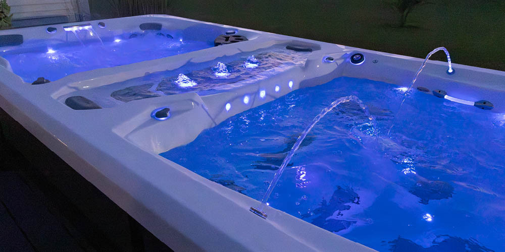 Vue nocturne d'un spa de nage avec jeux d'eau et éclairage LED allumé.