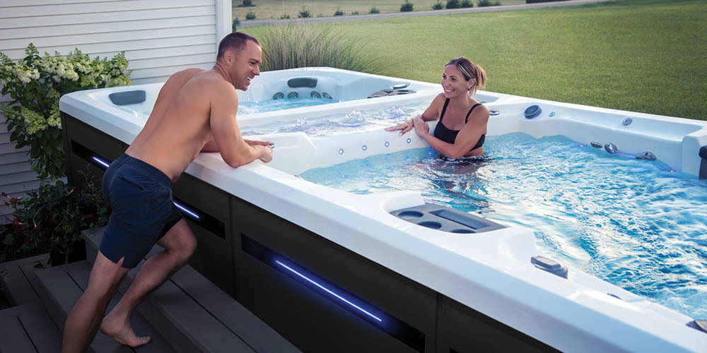 Un homme penché par-dessus le rebord d'un spa de nage H2X pour parler à une femme qui profite de l'eau.